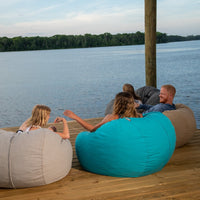 A family of three sits in outdoor bean bags on a dock. 