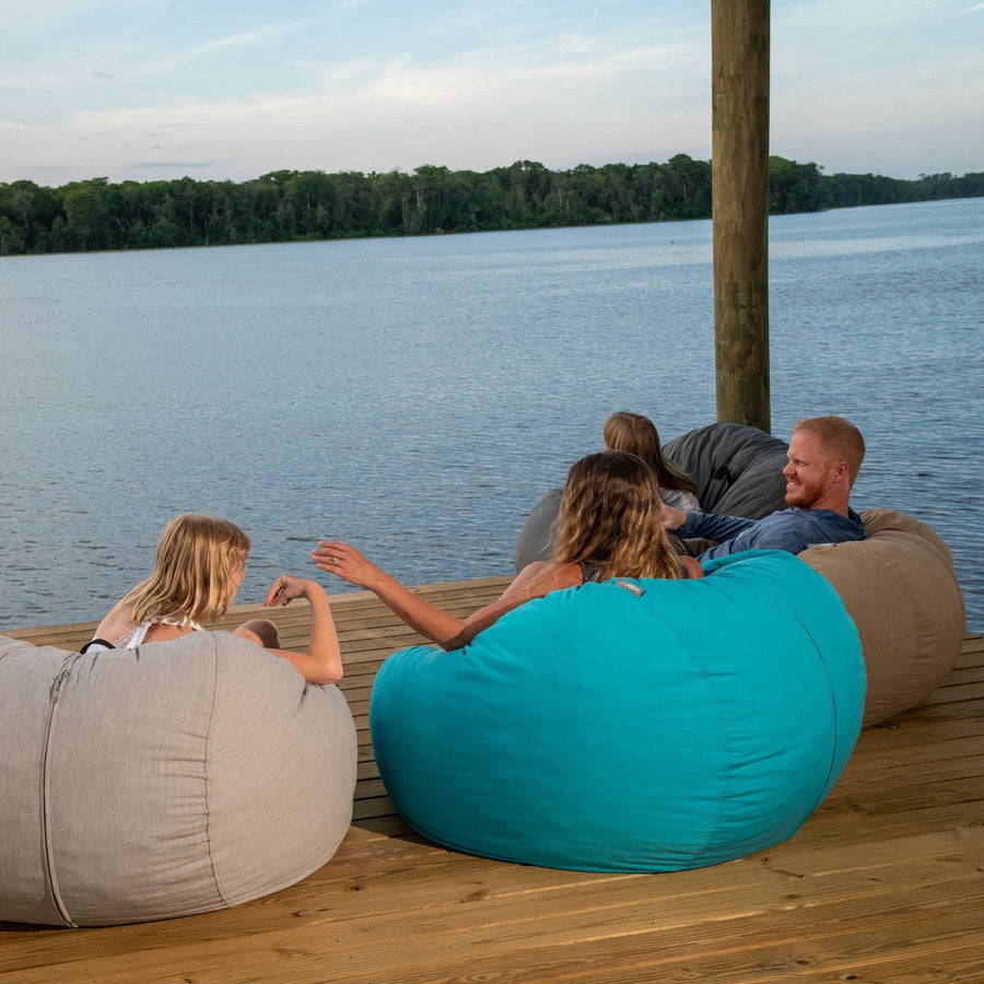 A family of three sits in outdoor bean bags on a dock. 