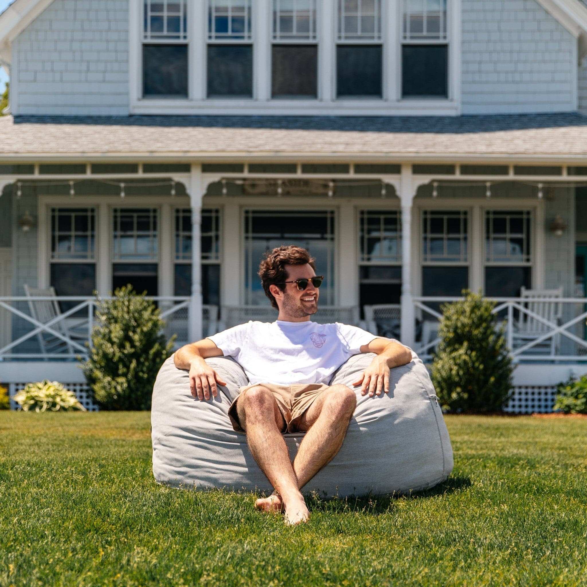 A man sits outside a house in a cordaroys outdoor bean bag in gray. 