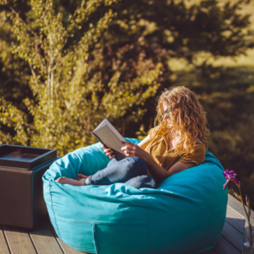 A woman reads a book outside on a cordaroys outdoor bean bag. 